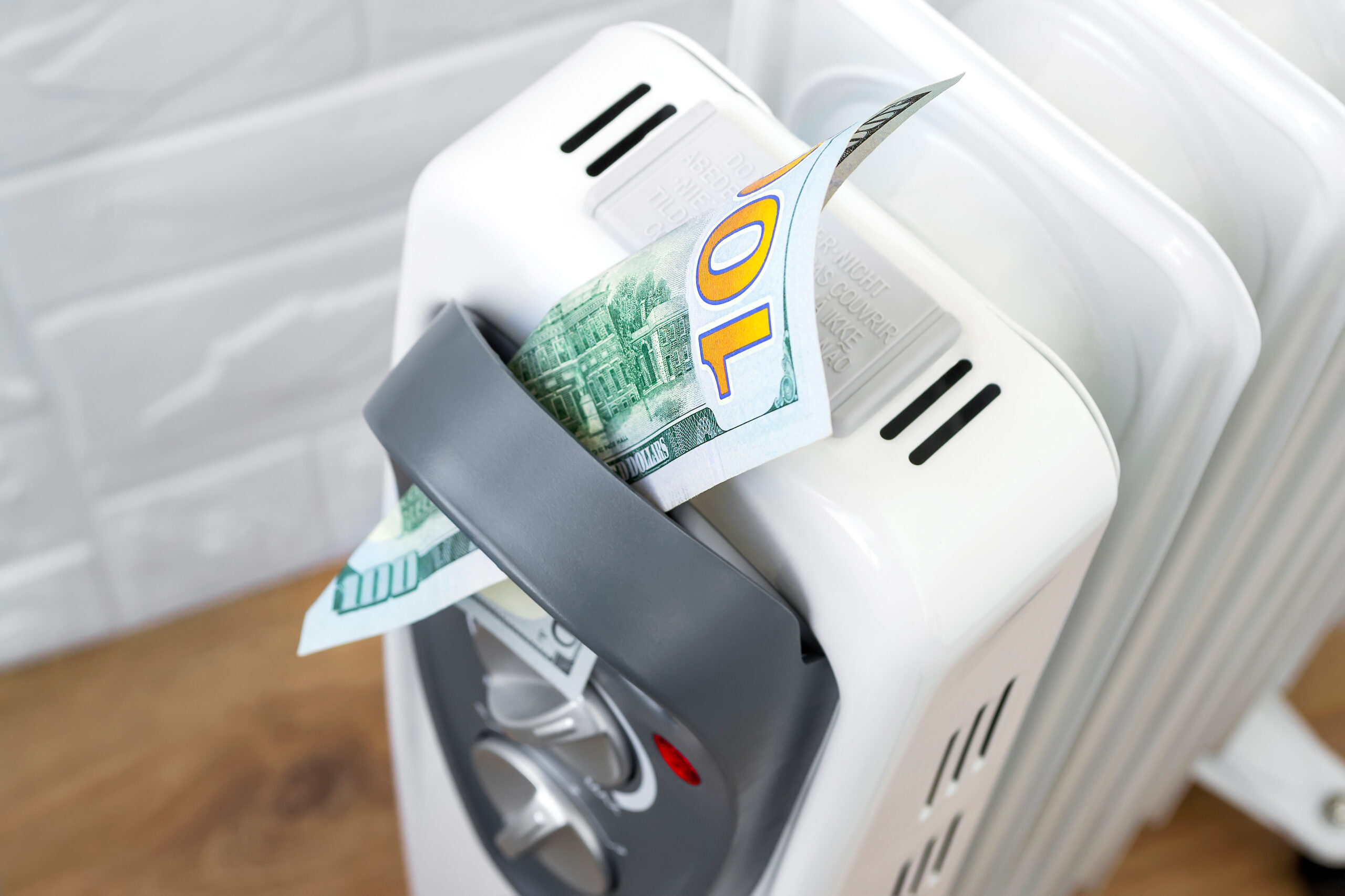 One hundred dollar bill in a handle of home electric oil radiator. Expensive electricity and higher electricity costs during the cold season concepts